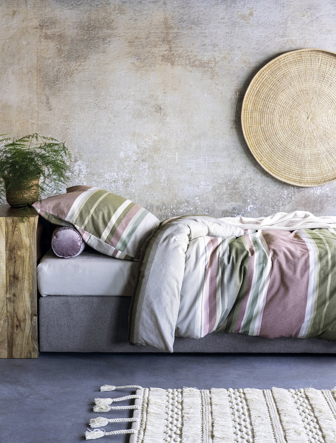 Auf einem Bett liegen mehrere Kopfkissen und eine Bettdecke bezogen mit Edel-Feinbiber Bettwaesche aus 100 Prozent Baumwolle mit Muster aus horizontalen Streifen in der Farbe Mehrfarbig. Modell Gestreift Gruen/Rosa.