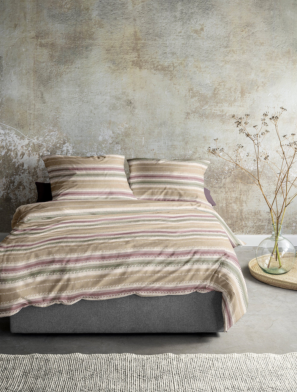 Auf einem Bett liegen mehrere Kopfkissen und eine Bettdecke bezogen mit Edel-Feinbiber Bettwaesche aus 100 Prozent Baumwolle mit Muster aus vertikalen Streifen in der Farbe Beige. Modell Sereno.