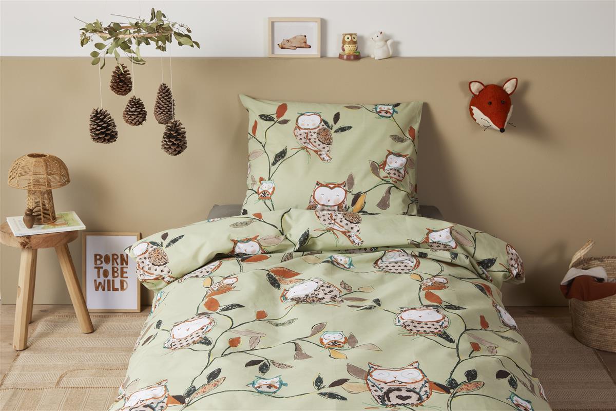 In einem Kinderzimmer steht ein Bett mit einem Kopfkissen und einer Bettdecke bezogen mit kuscheliger beddinghouse Bettwaesche aus 100 Prozent Baumwolle mit Illustrationen von Eulen in der Farbe Gruen. Modell Owls Green.