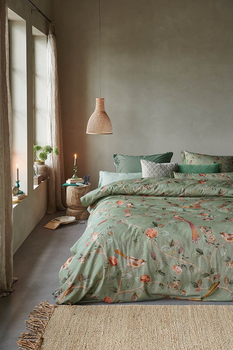 Auf einem Bett liegen mehrere Kopfkissen und eine Bettdecke bezogen mit Perkal-Baumwoll Bettwaesche aus 100 Prozent Baumwolle mit Muster aus Pflanzen und Voegeln in der Farbe Gruen. Modell Good Nightingale Light Green.