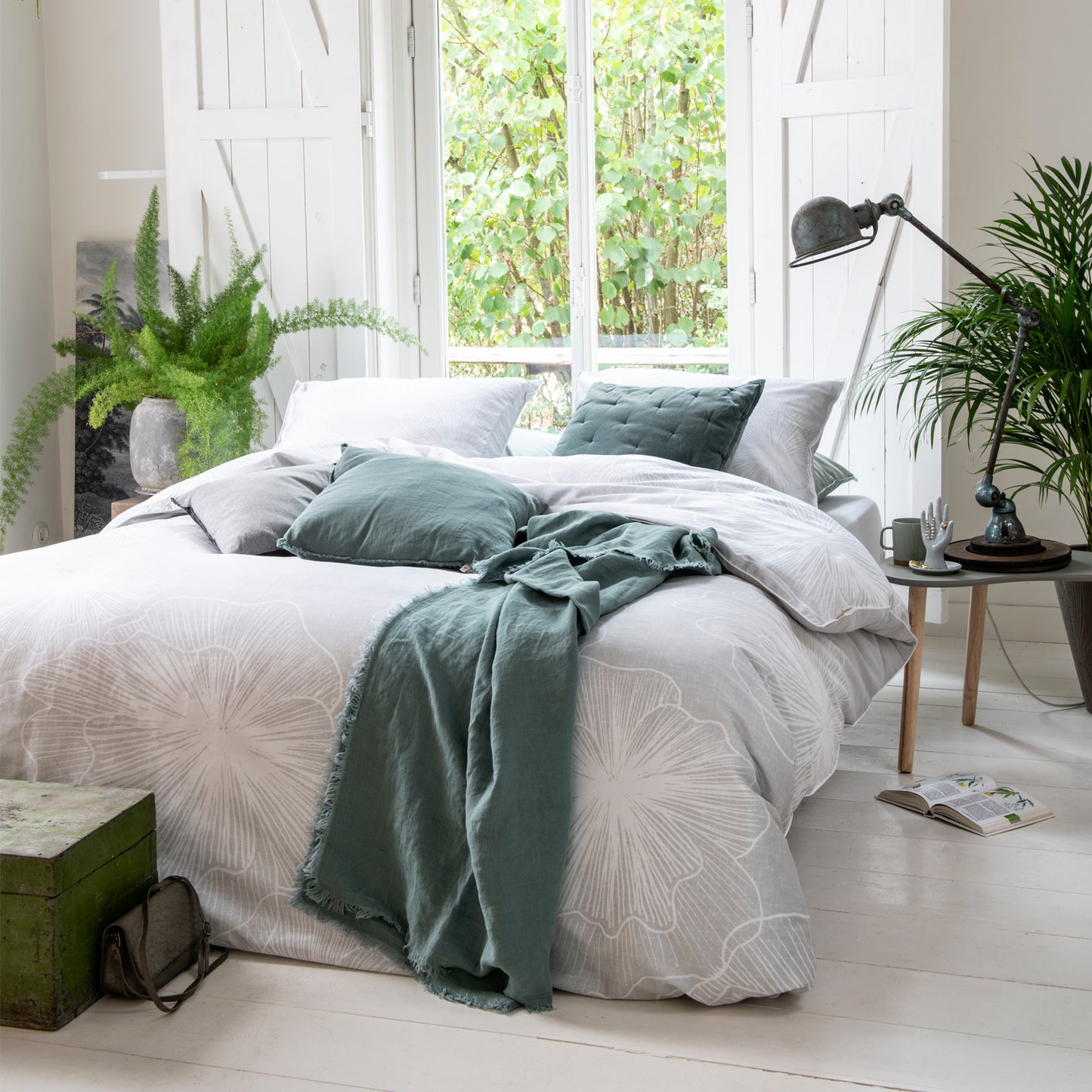 Auf einem Bett liegen mehrere Kopfkissen und eine Bettdecke bezogen mit Satin Bettwaesche aus 100 Prozent Baumwolle mit Muster aus Blueten in der Farbe Silber. Modell Fine Feston.