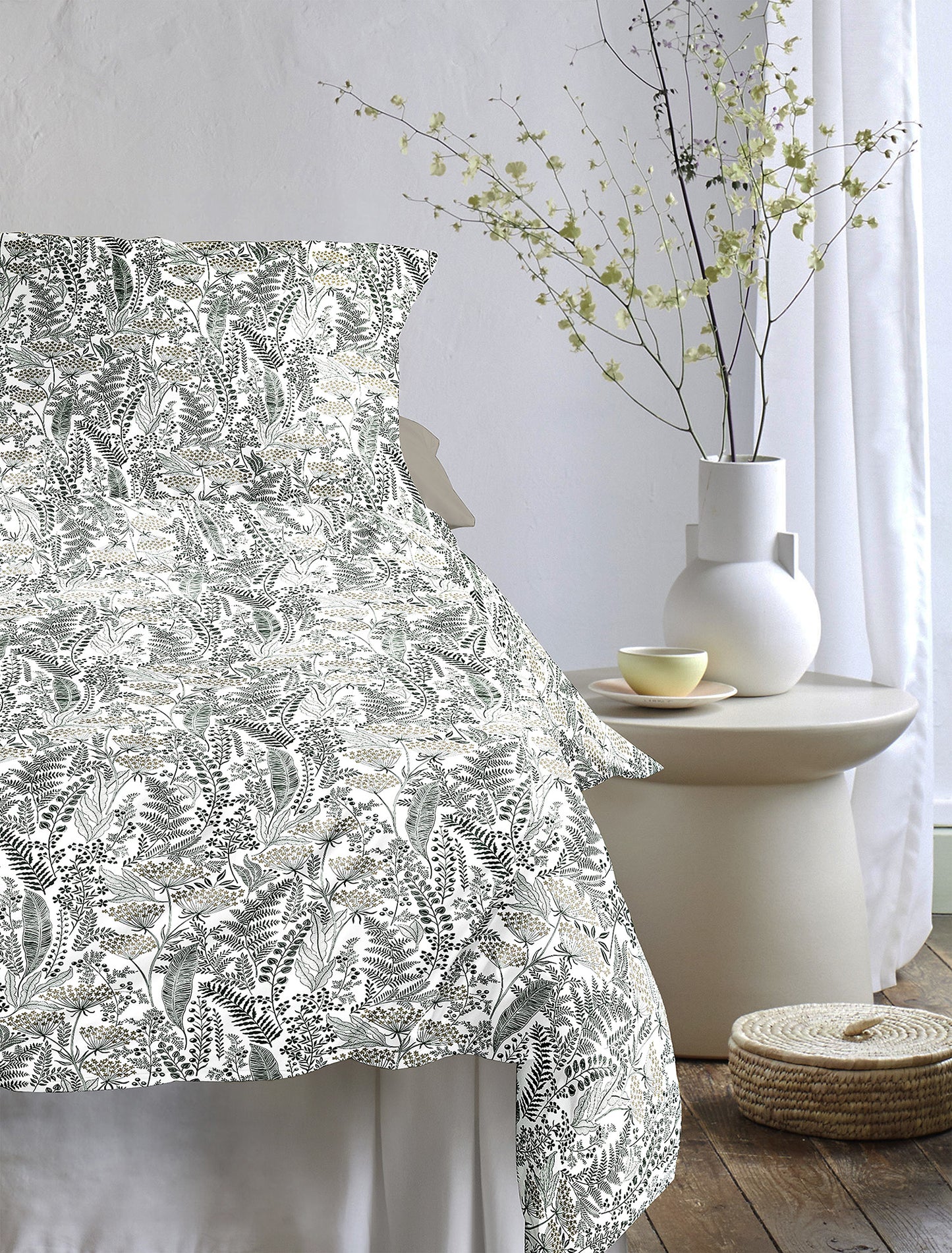 Auf einem Bett liegen mehrere Kopfkissen und eine Bettdecke bezogen mit Tencel-Lyocell Bettwaesche aus 100 Prozent Baumwolle mit Muster aus Blaettern in der Farbe Gruen. Modell Lotus Natur.