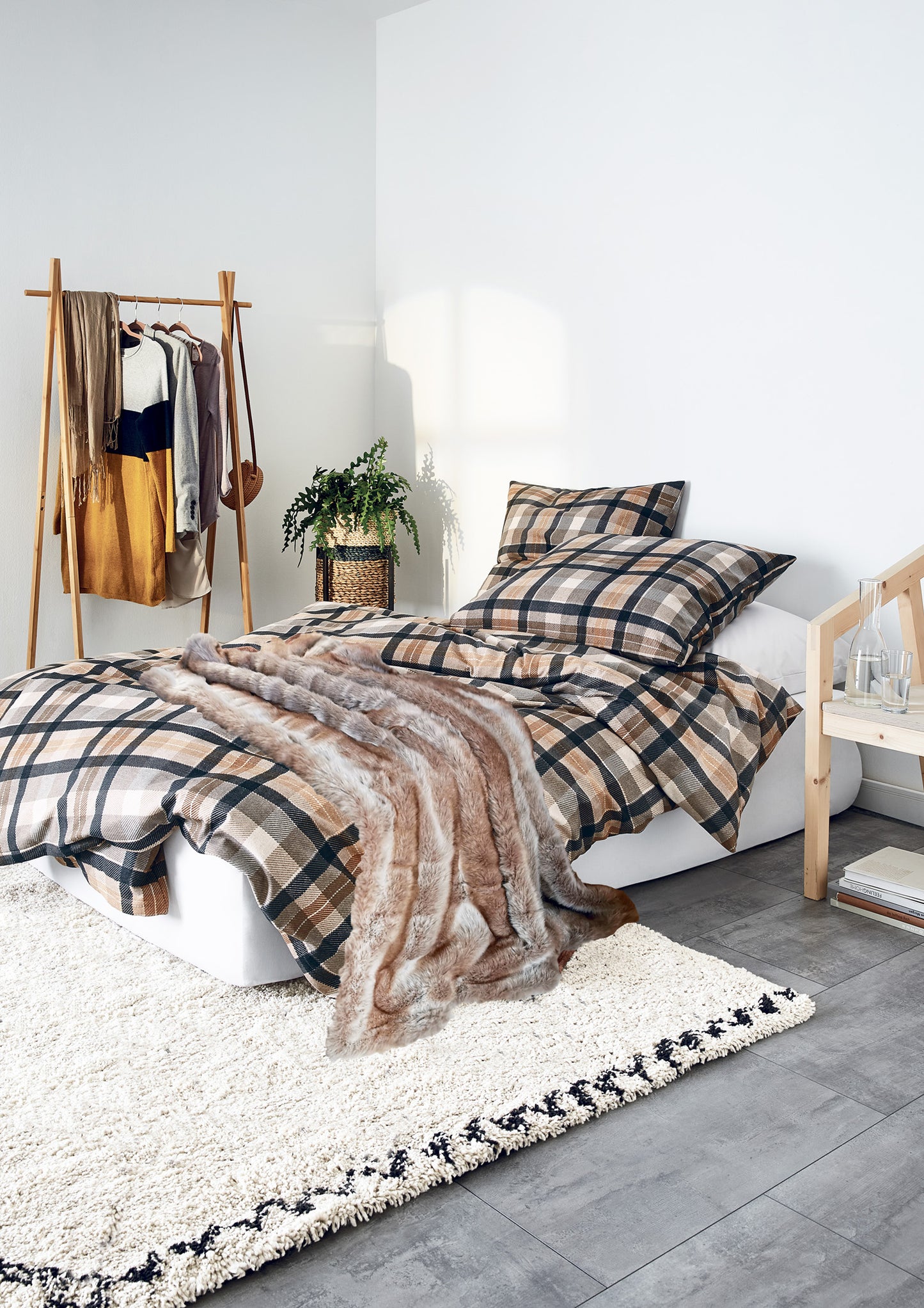 Auf einem Bett liegen mehrere Kopfkissen und eine Bettdecke bezogen mit Edel-Feinbiber Bettwaesche aus 100 Prozent Baumwolle mit Muster aus Quadraten in der Farbe Braun. Modell Koala Natur.