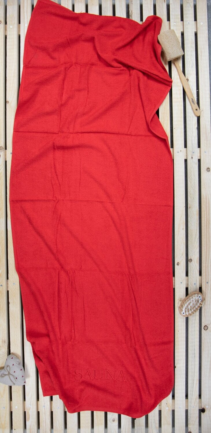 Auf einer Holzbankank liegt ein Saunatuch mit aufgesticktem Text SAUNA von p.k. aus 100 Prozent Baumwolle in der Groesse 70x200cm. Farbe Rot. Modell Rot.