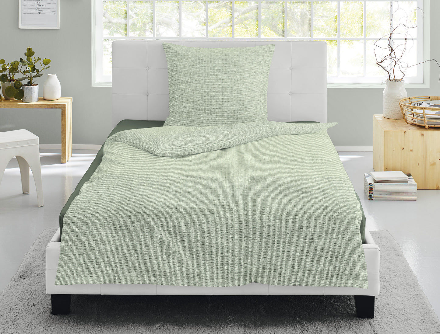Auf einem Bett liegen mehrere Kopfkissen und eine Bettdecke bezogen mit Soft Seersucker Bettwaesche aus 100 Prozent Baumwolle mit Muster aus graphischen Formen in der Farbe Gruen. Modell Easy Green.