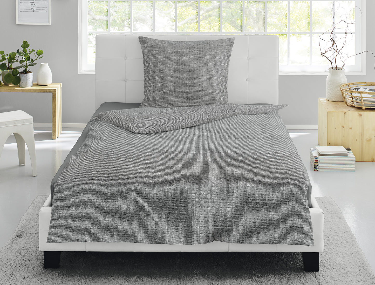 Auf einem Bett liegen mehrere Kopfkissen und eine Bettdecke bezogen mit Soft Seersucker Bettwaesche aus 100 Prozent Baumwolle mit Muster aus graphischen Formen in der Farbe Grau. Modell Easy Grey.