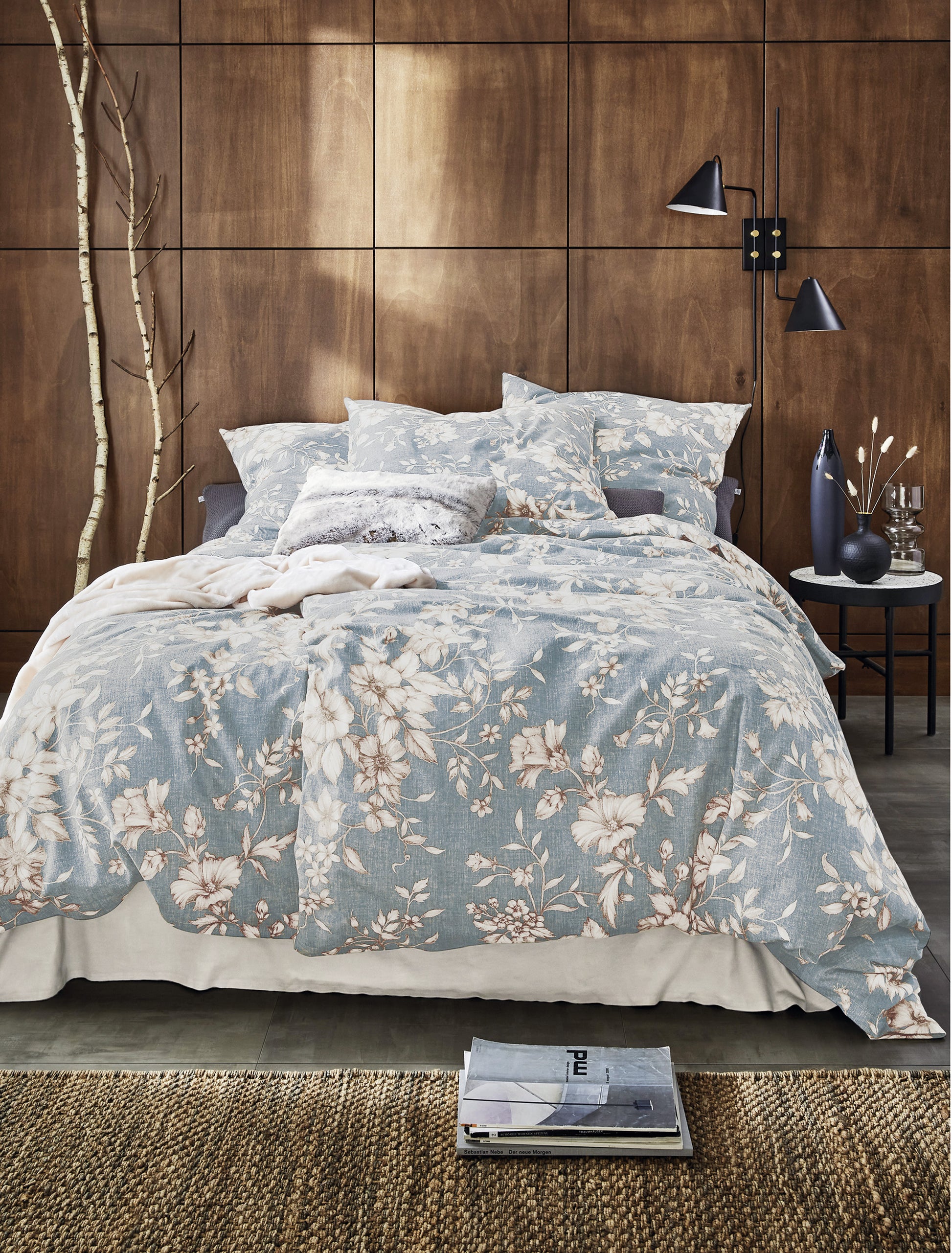 Auf einem Bett liegen mehrere Kopfkissen und eine Bettdecke bezogen mit Edel-Feinbiber Bettwaesche aus 100 Prozent Baumwolle mit Muster aus Blumen in der Farbe Blau. Modell Blumen.