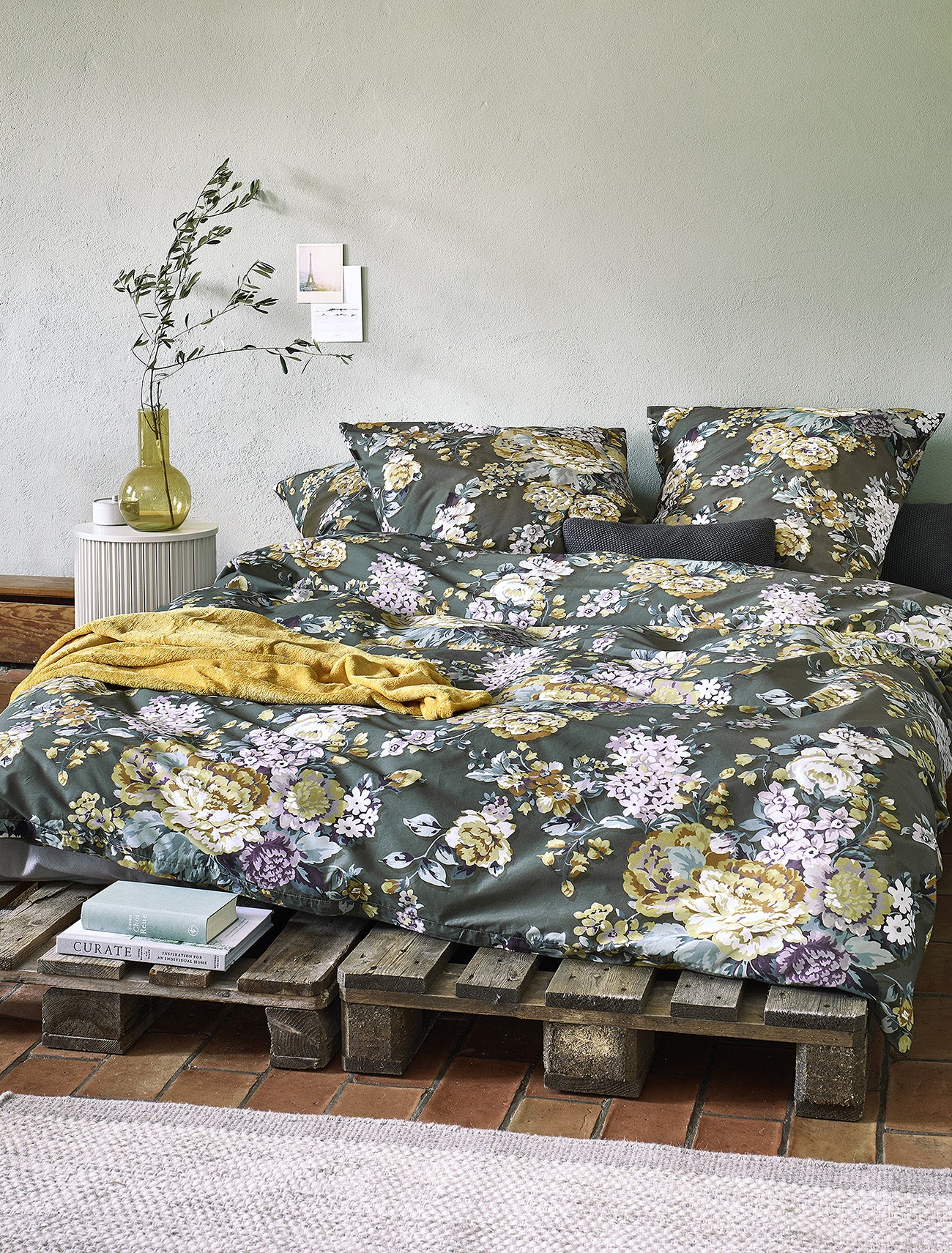 Auf einem Bett liegen mehrere Kopfkissen und eine Bettdecke bezogen mit Edel-Feinbiber Bettwaesche aus 100 Prozent Baumwolle mit Muster aus Blumen in der Farbe Gruen. Modell Blumen Gruen.