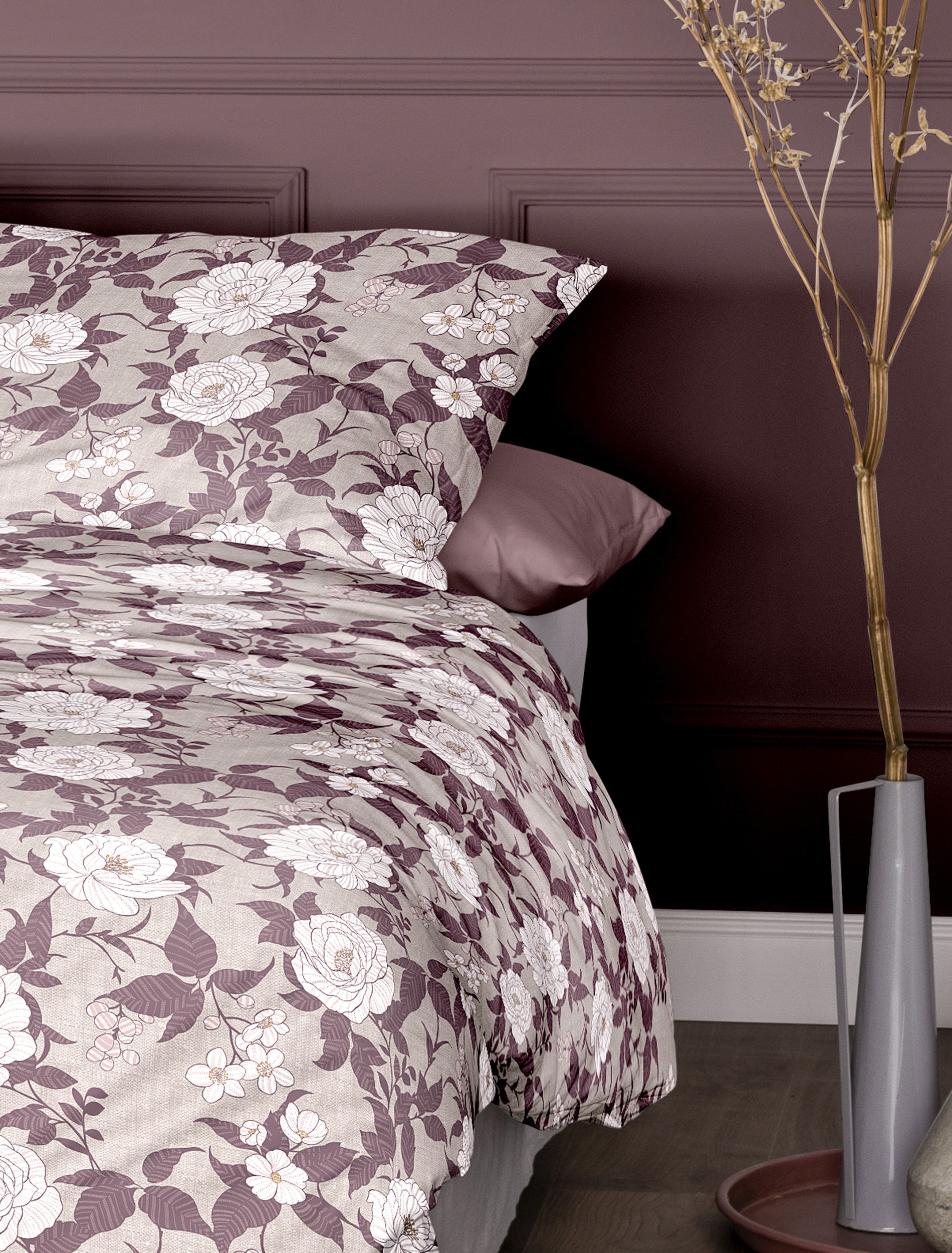 Auf einem Bett liegen mehrere Kopfkissen und eine Bettdecke bezogen mit Edel-Feinbiber Bettwaesche aus 100 Prozent Baumwolle mit Muster aus Blumen in der Farbe Rosa. Modell Florina Rosa.