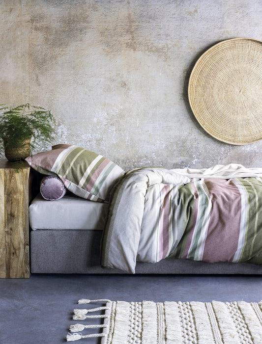 Auf einem Bett liegen mehrere Kopfkissen und eine Bettdecke bezogen mit Edel-Feinbiber Bettwaesche aus 100 Prozent Baumwolle mit Muster aus horizontalen Streifen in der Farbe Mehrfarbig. Modell Gestreift Gruen/Rosa.