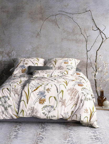 Auf einem Bett liegen mehrere Kopfkissen und eine Bettdecke bezogen mit Edel-Feinbiber Bettwaesche aus 100 Prozent Baumwolle mit Muster aus Graesern in der Farbe Weiss. Modell Graeser.