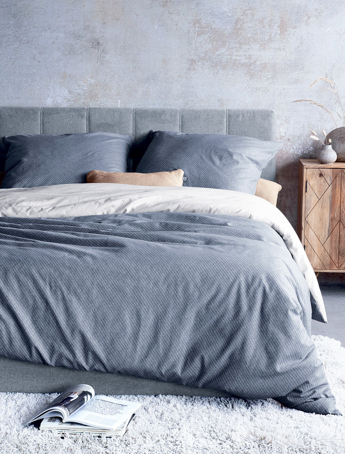 Auf einem Bett liegen mehrere Kopfkissen und eine Bettdecke bezogen mit Edel-Feinbiber Bettwaesche aus 100 Prozent Baumwolle mit Muster aus Linien in der Farbe Grau. Modell Grau.