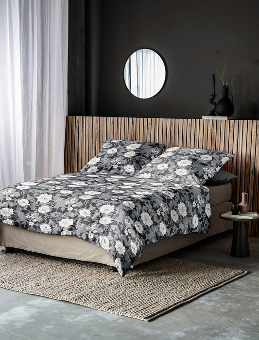 Auf einem Bett liegen mehrere Kopfkissen und eine Bettdecke bezogen mit Edel-Feinbiber Bettwaesche aus 100 Prozent Baumwolle mit Muster aus Blumen in der Farbe Grau. Modell Koala Grau.