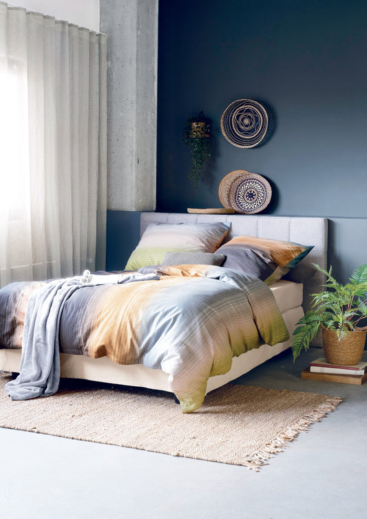 Auf einem Bett liegen mehrere Kopfkissen und eine Bettdecke bezogen mit Edel-Feinbiber Bettwaesche aus 100 Prozent Baumwolle mit Muster aus Streifen in der Farbe Mehrfarbig. Modell Orange/Gruen/Grau.