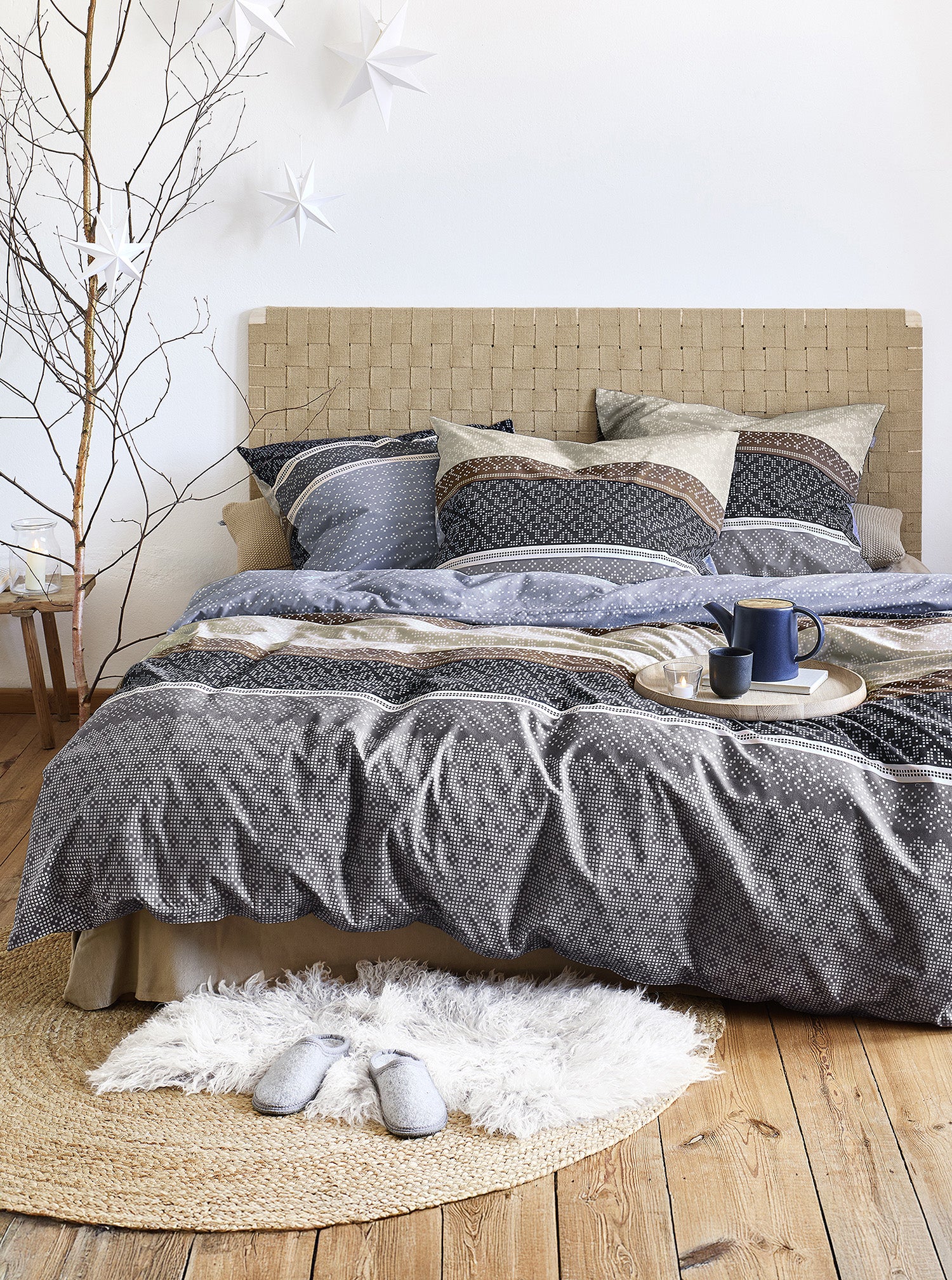 Auf einem Bett liegen mehrere Kopfkissen und eine Bettdecke bezogen mit Edel-Feinbiber Bettwaesche aus 100 Prozent Baumwolle mit Muster aus geographischen Formen in der Farbe Blau. Modell Panda Blau.