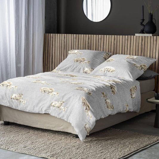 Auf einem Bett liegen mehrere Kopfkissen und eine Bettdecke bezogen mit Edel-Feinbiber Bettwaesche aus 100 Prozent Baumwolle mit Muster aus Schaefchen in der Farbe Grau. Modell Schaefchen Grau.