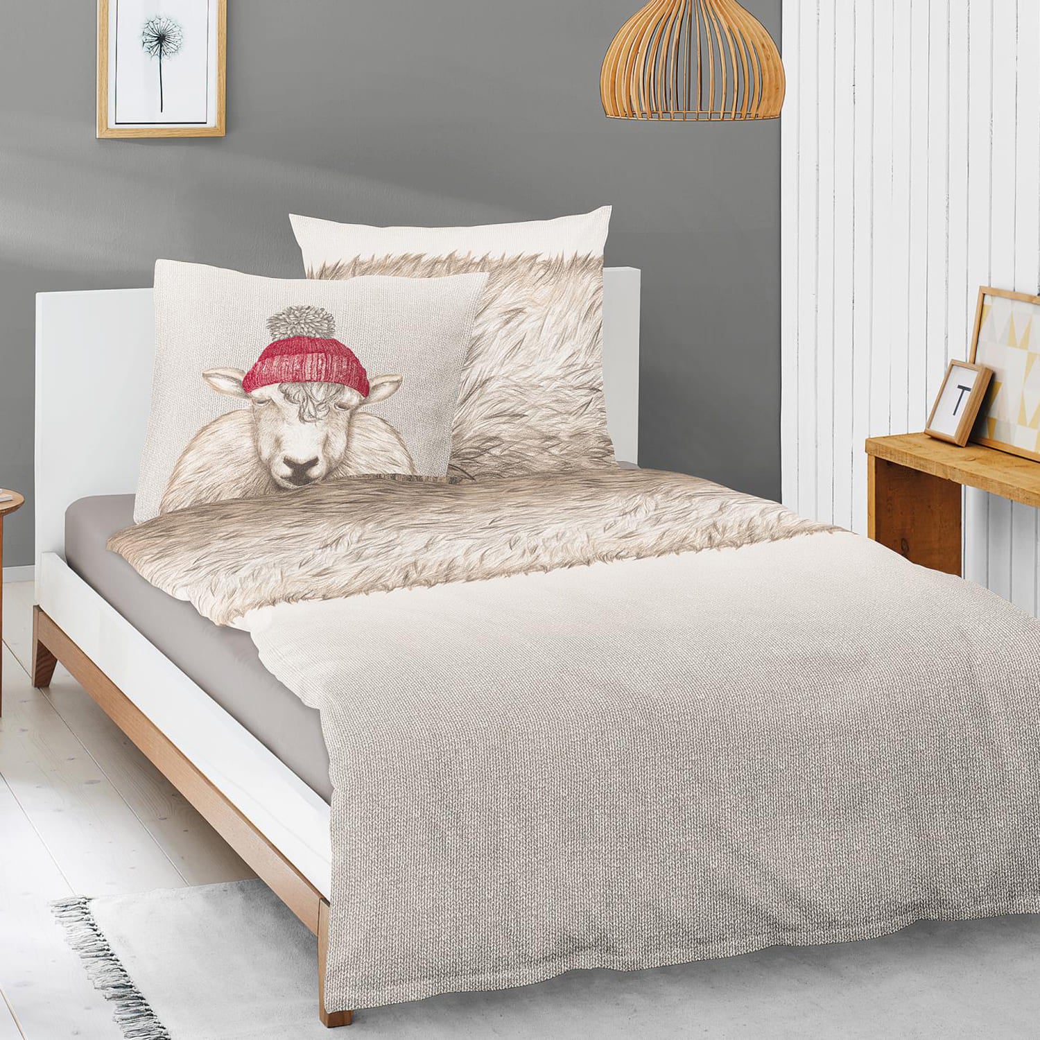 Auf einem Bett liegen mehrere Kopfkissen und eine Bettdecke bezogen mit Edel-Feinbiber Bettwaesche aus 100 Prozent Baumwolle mit Muster aus Schafen und Schafsfell in der Farbe Beige. Modell Schaf Grau.