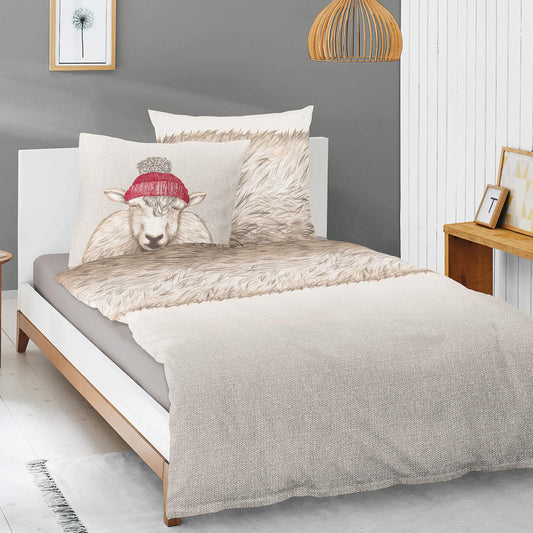 Auf einem Bett liegen mehrere Kopfkissen und eine Bettdecke bezogen mit Edel-Feinbiber Bettwaesche aus 100 Prozent Baumwolle mit Muster aus Schafen und Schafsfell in der Farbe Beige. Modell Schaf Grau.