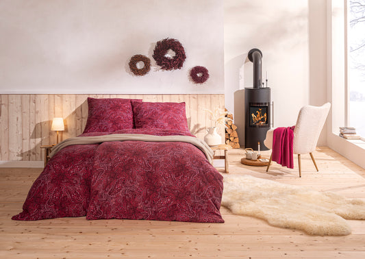 Ein Bettbezug-Set aus mehreren Kopfkissen und einer Bettdecke bezogen mit Edel-Flanell Bettwaesche aus 100 Prozent Baumwolle mit Muster aus Blueten in der Farbe Rot. Modell Paola Purpur.