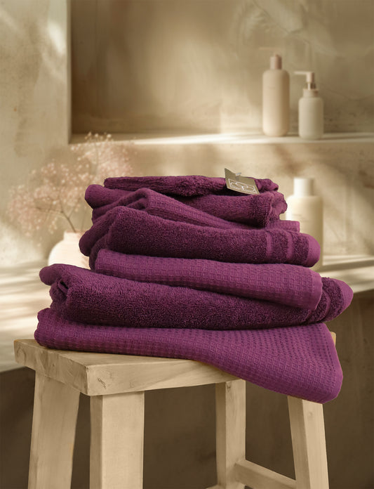 Ein Stapel aus mehreren Handtuechern die aufeinander liegen in der Farbe Lila. Modell Waffelpique Plum. 