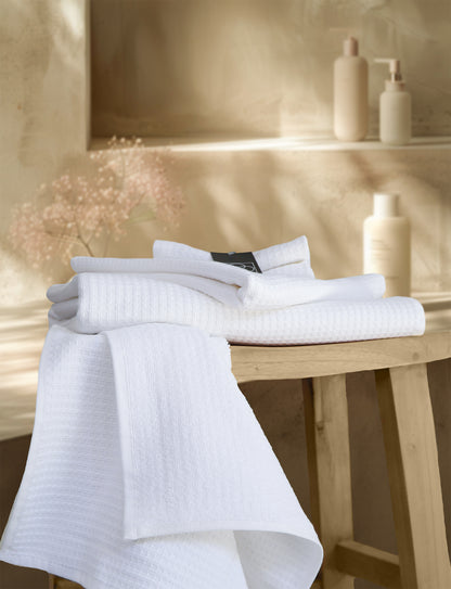 Ein Stapel aus mehreren Handtuechern die aufeinander liegen in der Farbe Weiss. Modell Waffelpique Weiss. 