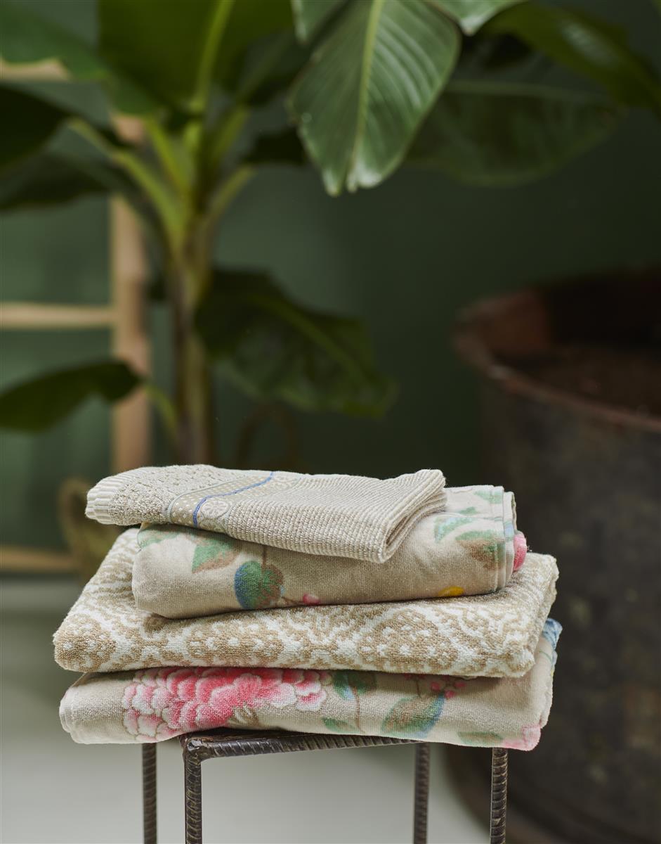 Auf einem Stuhl liegt ein Stapel aus mehreren Handtuechern in verschiedenen Groessen von PIP STUDIO die aufeinander liegen mit Muster aus Blumen in der Farbe Taupe. Modell Good Evening Khaki.