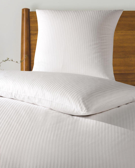 Auf einem Bett liegt ein Kopfkissen und eine Bettdecke bezogen mit Bettwaesche aus 100 Prozent Baumwolle mit Muster aus vertikalen Streifen in der Farbe Weiss. Modell Streifen Weiss.
