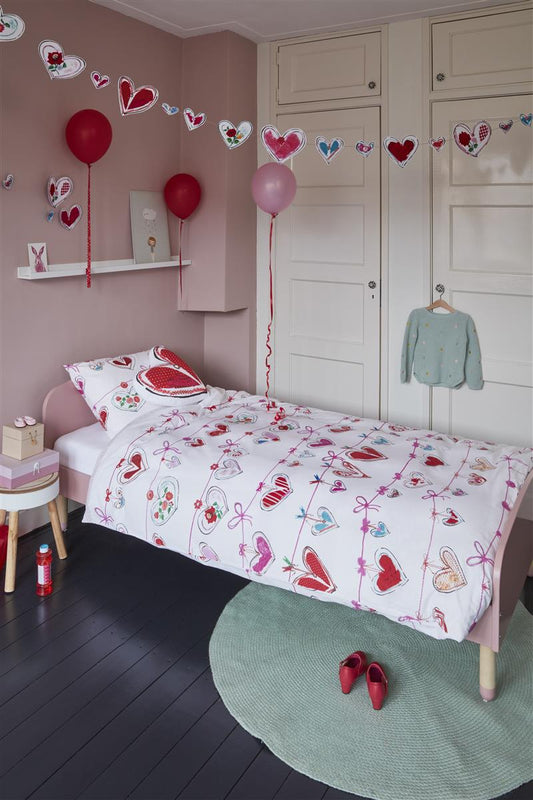 In einem Kinderzimmer steht ein Kinderbett mit einem Kopfkissen und einer Bettdecke bezogen mit kuscheliger beddinghouse Bettwaesche aus 100 Prozent Baumwolle mit Illustrationen von Herzen in der Farbe Weiss. Modell Hearts.