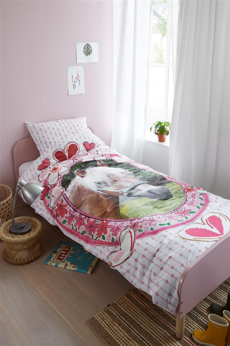 In einem Kinderzimmer steht ein Kinderbett mit einem Kopfkissen und einer Bettdecke bezogen mit kuscheliger beddinghouse Bettwaesche aus 100 Prozent Baumwolle mit Illustrationen von Herzen und Pferden in der Farbe Weiss. Modell Horse Hearts