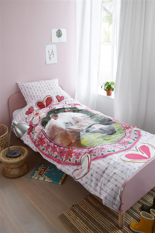 In einem Kinderzimmer steht ein Kinderbett mit einem Kopfkissen und einer Bettdecke bezogen mit kuscheliger beddinghouse Bettwaesche aus 100 Prozent Baumwolle mit Illustrationen von Herzen und Pferden in der Farbe Weiss. Modell Horse Hearts