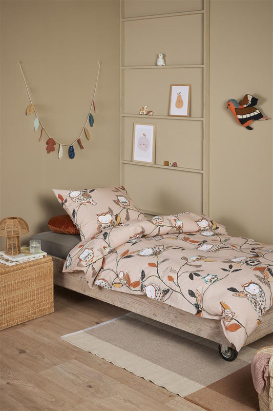 In einem Kinderzimmer steht ein Kinderbett mit einem Kopfkissen und einer Bettdecke bezogen mit kuscheliger beddinghouse Bettwaesche aus 100 Prozent Baumwolle mit Illustrationen von Eulen in der Farbe Beige. Modell Owls Beige.