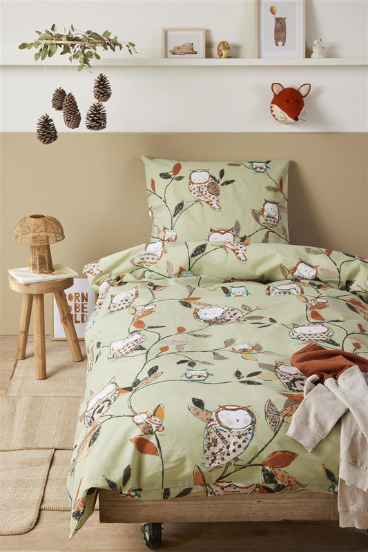 In einem Kinderzimmer steht ein Kinderbett mit einem Kopfkissen und einer Bettdecke bezogen mit kuscheliger beddinghouse Bettwaesche aus 100 Prozent Baumwolle mit Illustrationen von Eulen in der Farbe Gruen. Modell Owls Green.