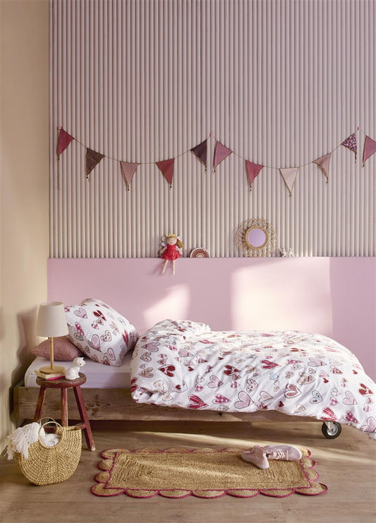 In einem Kinderzimmer steht ein Kinderbett mit einem Kopfkissen und einer Bettdecke bezogen mit kuscheliger beddinghouse Bettwaesche aus 100 Prozent Baumwolle mit Illustrationen von Herzen in der Farbe Weiss. Modell Sweethearts.