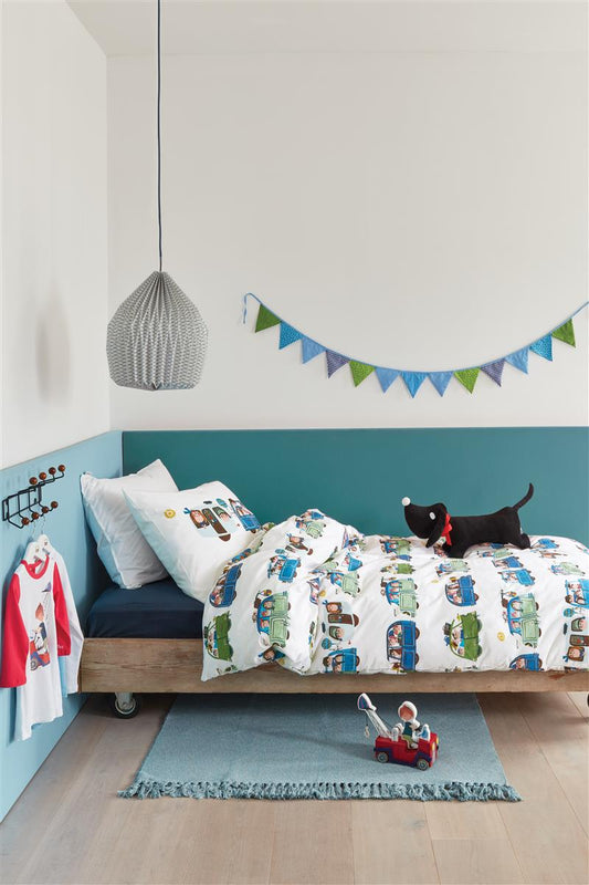 In einem Kinderzimmer steht ein Kinderbett mit einem Kopfkissen und einer Bettdecke bezogen mit kuscheliger beddinghouse Bettwaesche aus 100 Prozent Baumwolle mit Illustrationen von Autos und Wohnwagen in der Farbe Weiss. Modell Vakantie.
