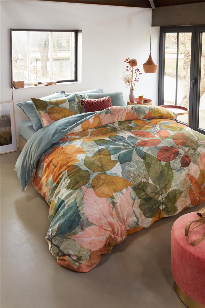 In einem Schlafzimmer steht ein Bett mit mehreren Kopfkissen und einer Bettdecke bezogen mit kuscheliger beddinghouse Mako-Satin Bettwaesche aus 100 Prozent Baumwolle mit Illustrationen von Blaettern in der Farbe Mehrfarbig. Modell Autum Multi.