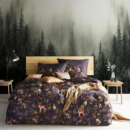 Auf einem Bett liegen mehrere Kopfkissen und eine Bettdecke bezogen mit Mako-Satin Bettwaesche aus 100 Prozent Baumwolle mit Muster aus Waldtieren und Pflanzen in der Farbe Lila. Modell Forest.