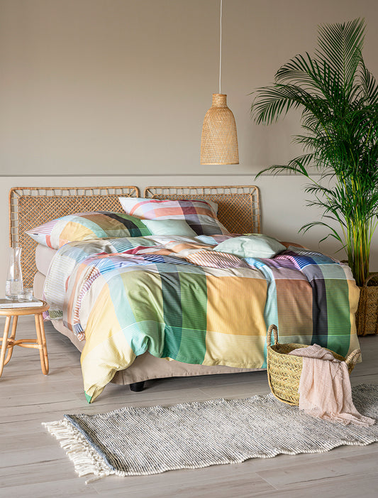 Auf einem Bett liegen mehrere Kopfkissen und eine Bettdecke bezogen mit Mako-Satin Bettwaesche aus 100 Prozent Baumwolle mit Muster aus Quadraten in der Farbe Mehrfarbig. Modell Coloria.