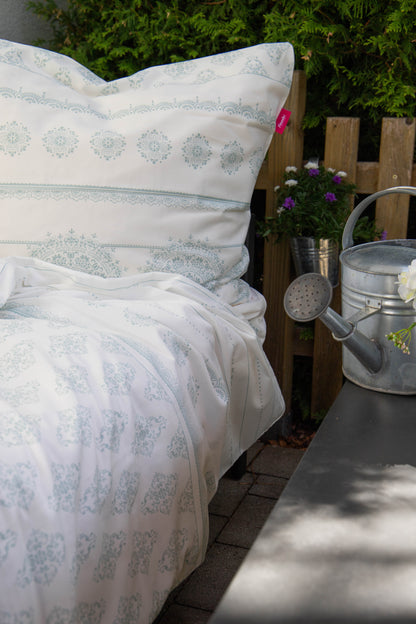 Auf einem Bett liegt ein Kopfkissen und eine Bettdecke bezogen mit Mako-Satin Bettwaesche aus 100 Prozent Baumwolle mit Muster aus geografischen Formen in der Farbe Weiss. Modell Freundin Home Collection Mint.