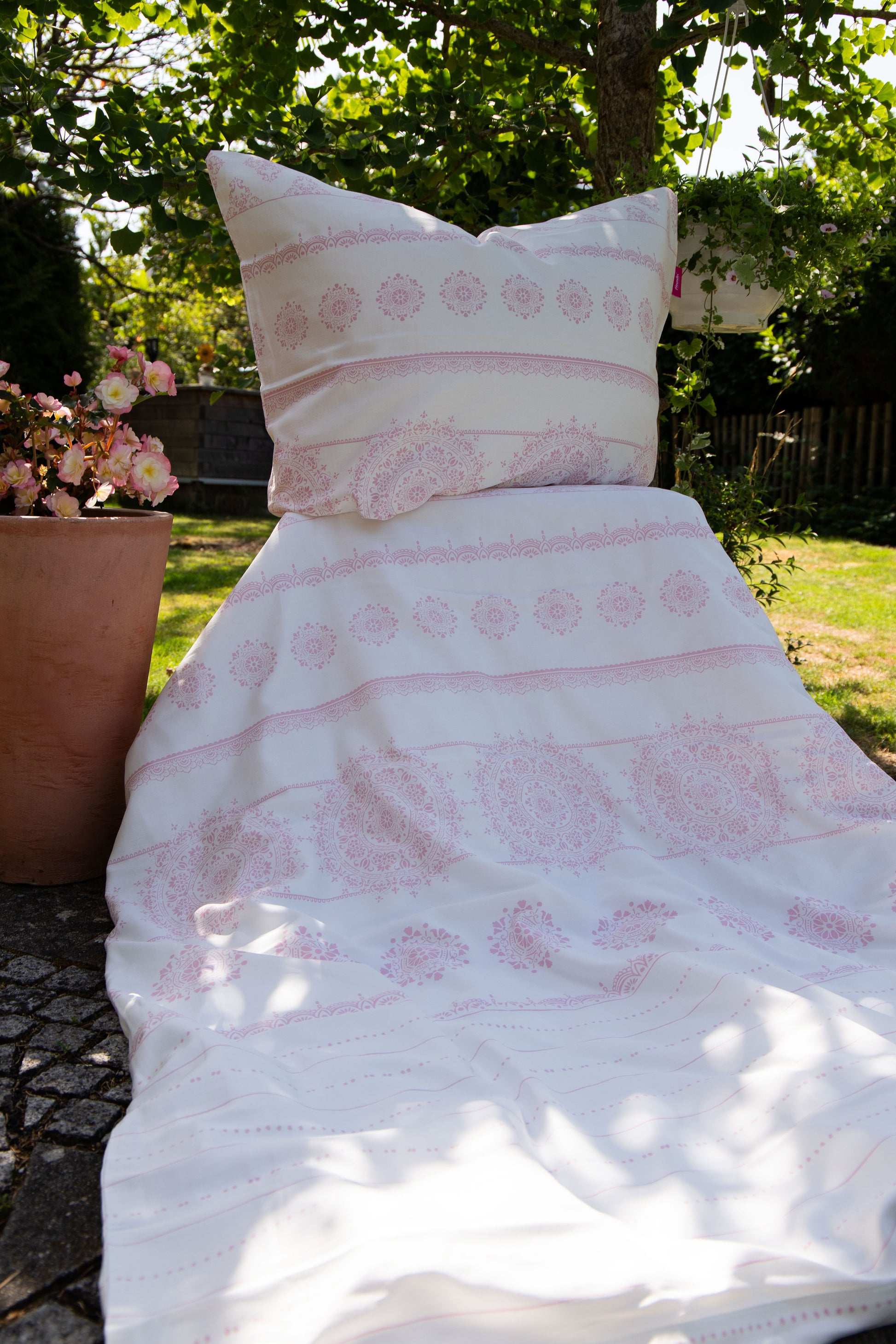 Auf einem Bett liegt ein Kopfkissen und eine Bettdecke bezogen mit Mako-Satin Bettwaesche aus 100 Prozent Baumwolle mit Muster aus geografischen Formen in der Farbe Weiss. Modell Freundin Home Collection Rosa.