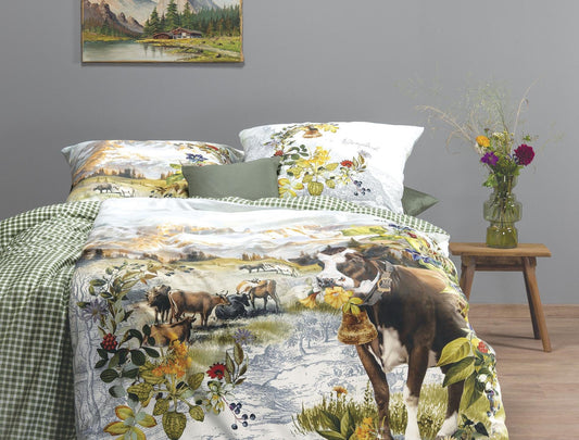Auf einem Bett liegen mehrere Kopfkissen und eine Bettdecke bezogen mit Mako-Satin Bettwaesche aus 100 Prozent Baumwolle mit Muster aus Alpenlandschaft in der Farbe Gruen. Modell Magic Alpenglueck.