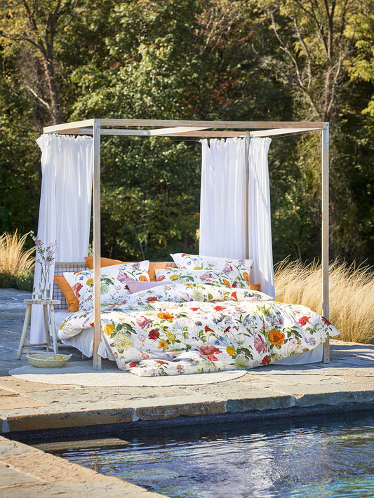 Auf einem Bett liegen mehrere Kopfkissen und eine Bettdecke bezogen mit Mako-Satin Bettwaesche aus 100 Prozent Baumwolle mit Muster aus Blumen in der Farbe Weiss. Modell Sky.