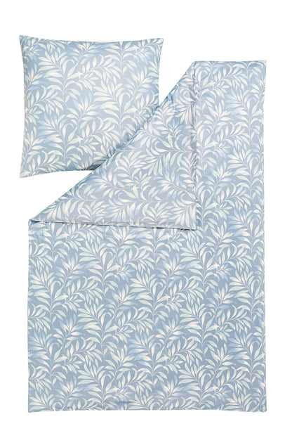 Ein Kopfkissen und eine Bettdecke bezogen mit Mako-Interlock-Jersey Bettwaesche mit einem Muster aus Blaettern in der Farbe Blau. Modell Elif Taube.