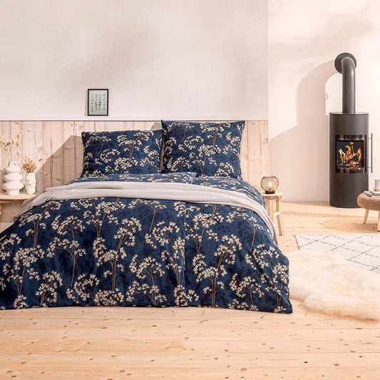 Ein Bettbezug-Set aus mehreren Kopfkissen und einer Bettdecke bezogen mit Mako-Interlock-Jersey Bettwaesche aus 100 Prozent Baumwolle mit Muster aus Blaettern in der Farbe Blau. Modell Riona Nachtblau.