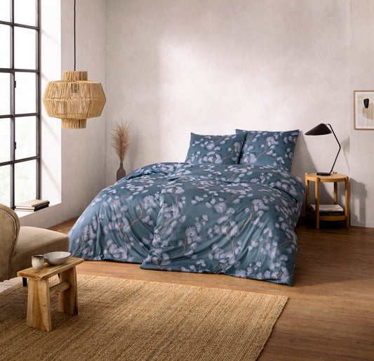 Ein Bettbezug-Set aus mehreren Kopfkissen und einer Bettdecke bezogen mit Mako-Interlock-Jersey Bettwaesche aus 100 Prozent Baumwolle mit Muster aus Blueten in der Farbe Blau. Modell Rumi Moos.