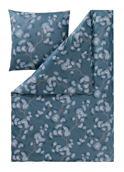 Ein Kopfkissen und eine Bettdecke bezogen mit Mako-Interlock-Jersey Bettwaesche mit einem Muster aus Blueten in der Farbe Blau. Modell Rumi Moos.