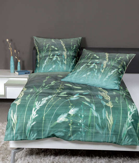 Auf einem Bett liegen mehrere Kopfkissen und eine Bettdecke bezogen mit Mako-Satin Bettwaesche aus 100 Prozent Baumwolle mit Muster aus Graesern in der Farbe Gruen. Modell Modern Art Green.