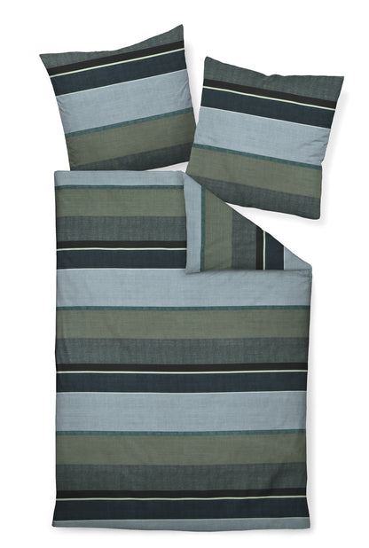 Zwei Kopfkissen und eine Bettdecke bezogen mit Mako-Satin Bettwaesche mit einem Muster aus horizontalen Streifen in der Farbe Blau. Modell Moments Blue.