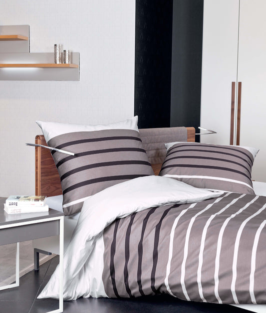 Auf einem Bett liegen mehrere Kopfkissen und eine Bettdecke bezogen mit Mako-Satin Bettwaesche aus 100 Prozent Baumwolle mit Muster aus horizontalen Streifen in der Farbe Mehrfarbig. Modell Palermo Lineo.
