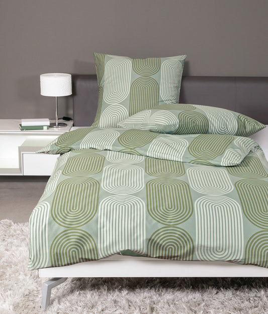 Auf einem Bett liegen mehrere Kopfkissen und eine Bettdecke bezogen mit Mako-Satin Bettwaesche aus 100 Prozent Baumwolle mit Muster aus grafischen Formen in der Farbe Gruen. Modell Rauchgrün Lind.