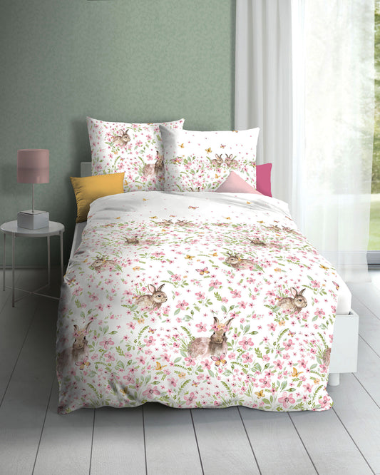 Auf einem Bett liegen mehrere Kopfkissen und eine Bettdecke bezogen mit Mako-Satin Bettwaesche aus 100 Prozent Baumwolle mit Muster aus Hasen in der Farbe Weiss. Modell Haeschen.